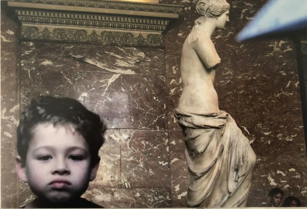 Young boy smirks in front of Venus di Milo in the Lourve