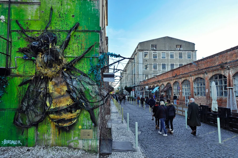 View of the Rua Rodrigues de Faria in the LX Factory community space with street art on the wall of a building in the foreground
