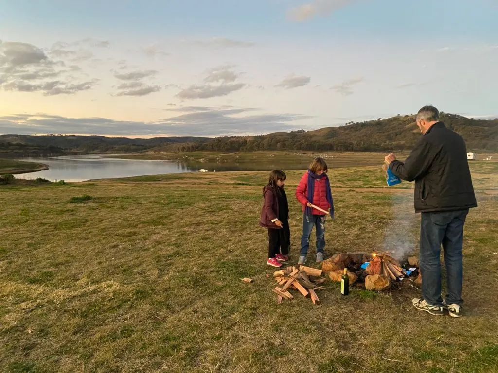 2 kids and a man setting a camp fire in an open field
