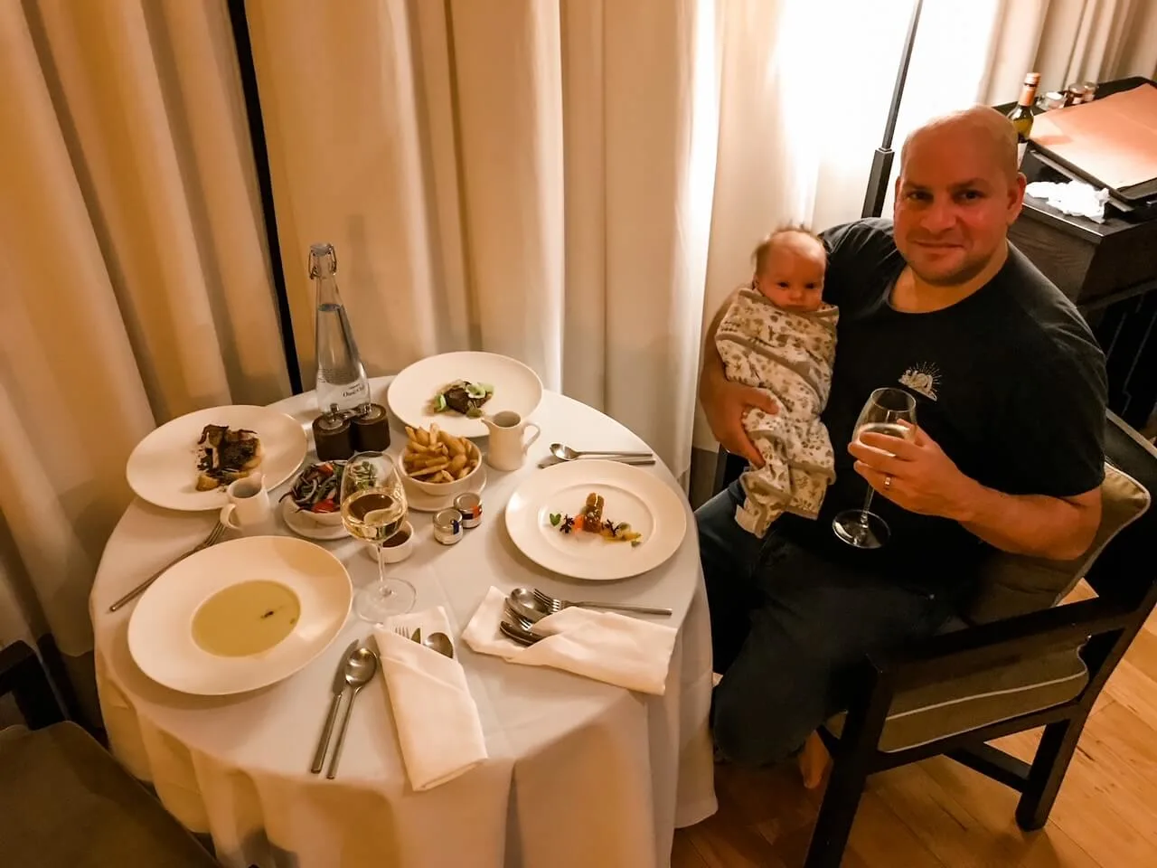 man holding a glass of wine and a tiny baby having in room dining at Emirates One&Only Wolgan Vally